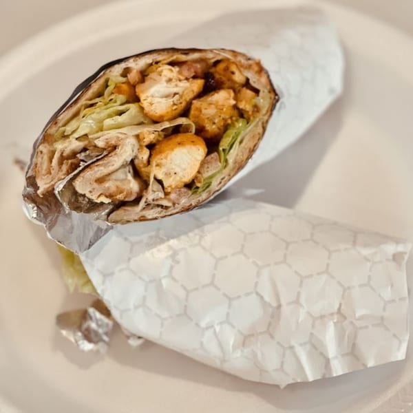 A chicken kebab wrap, partially unwrapped, revealing chicken, lettuce, and sauce.