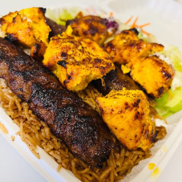 Grilled chicken and beef kabobs over rice with a side salad in a white takeout container.
