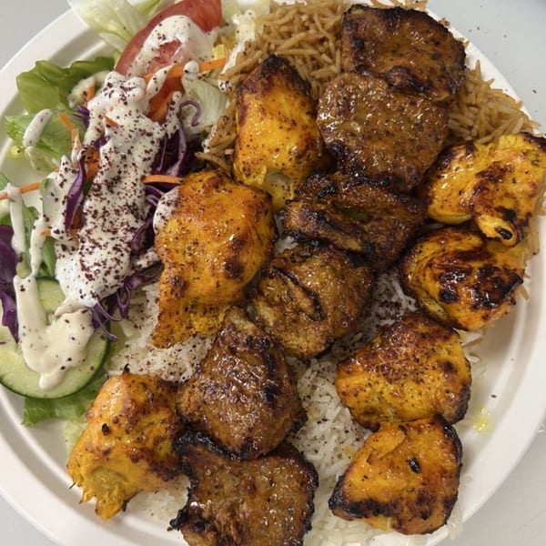 A plate of Grill Kabob's chicken and beef kebabs, rice, and a fresh salad with dressing.