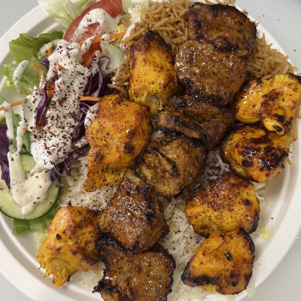A plate of Grill Kabob's chicken and beef kebabs, rice, and a fresh salad with dressing.
